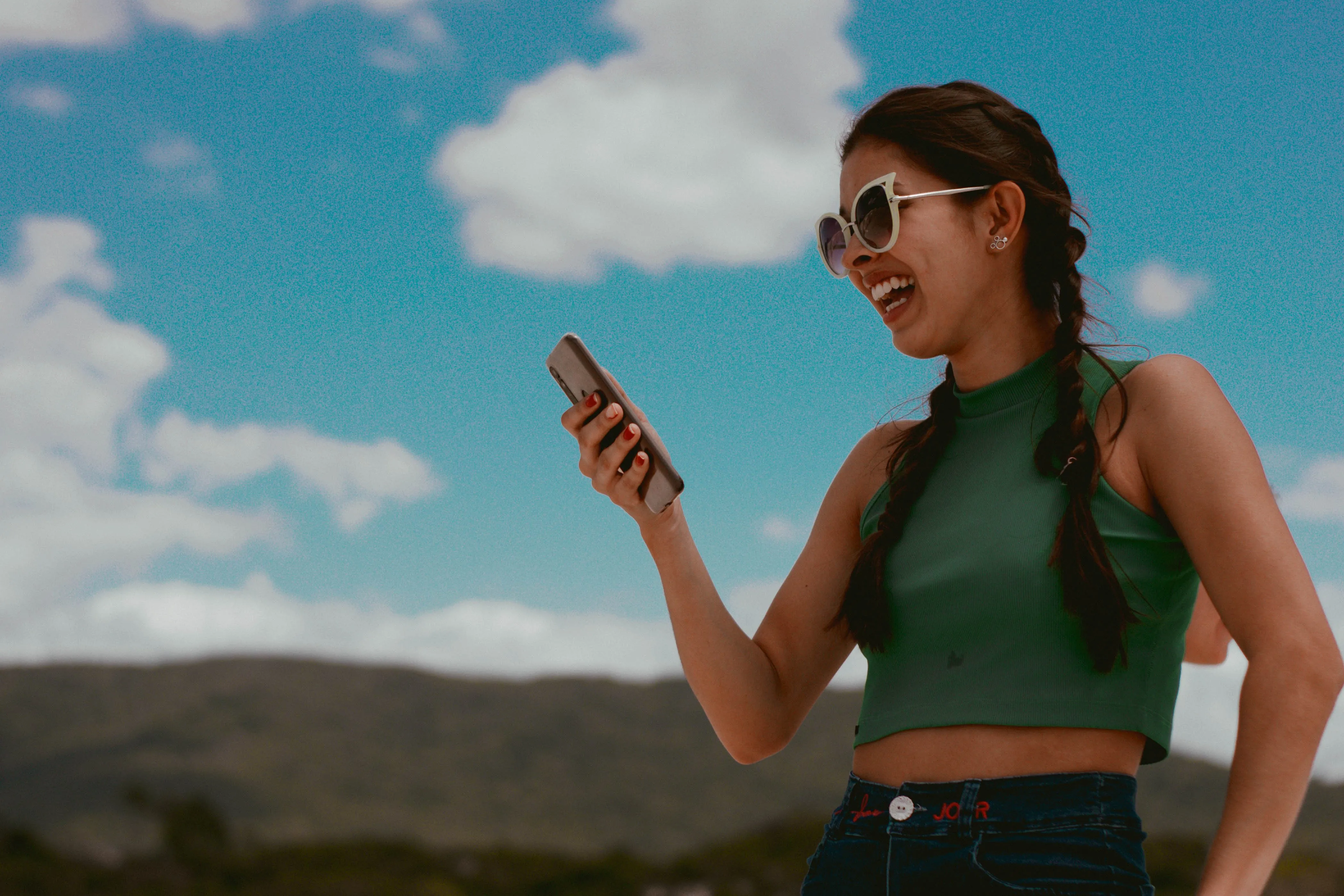 Vrouw lachend buiten met telefoon in hand