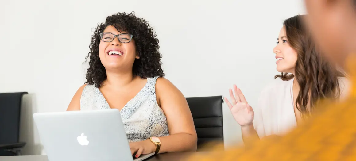 Twee vrouwen die lachen aan tafel met laptop