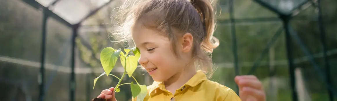 Meisje met gele blouse ruikt aan bloem in kas