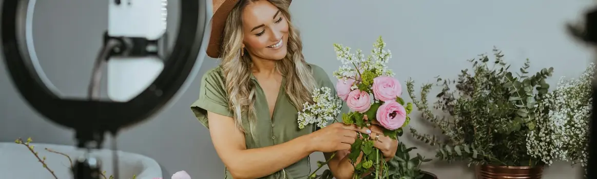 Vrouw schikt bloemen voor camera op standaard en ringlight
