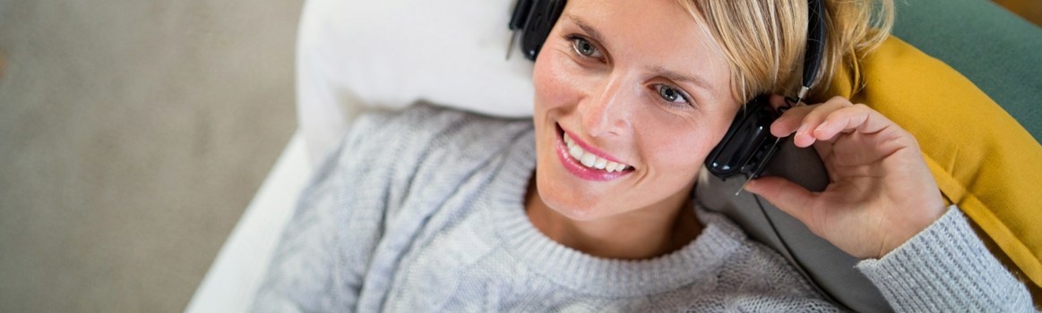 Vrouw luistert ontspannen naar audio via koptelefoon op de bank