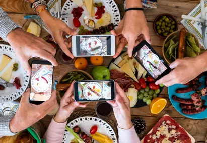 Bovenaanzicht van vier telefoons die een foto maken van een gedekte tafel vol eten en drinken