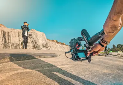Man in zwarte kleding op het strand wordt vastgelegd door een ander persoon met camera in de hand