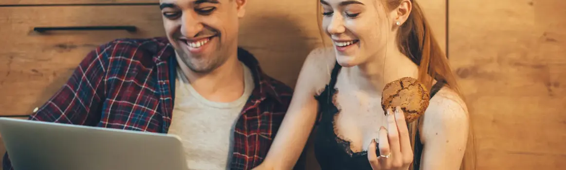 Man en vrouw achter laptop en vrouw eet een koekje