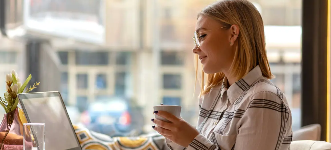 Vrouw aan tafel achter laptop met witte mok